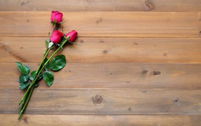 Три красные розы лежат на деревянном столе 