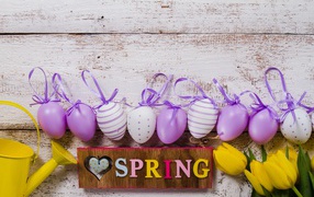 Multi-colored eggs, a bouquet of tulips and the inscription spring on a wooden background