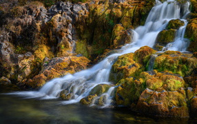 Rapid water of a waterfall flows over moss-covered stones, Iceland