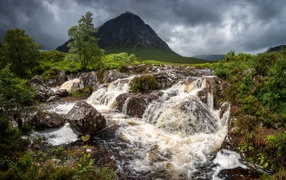 Waterfall flows down the stones near the mountain against the backdrop of a stormy sky