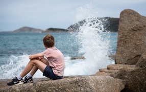 A boy sits on stones by the raging sea