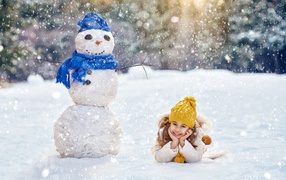 Милая девочка лежит на снегу у снеговика зимой