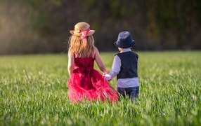 Маленькие мальчик и девочка идут по зеленому полю