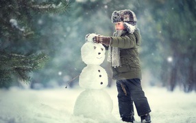 Little boy sculpts a snowman in winter