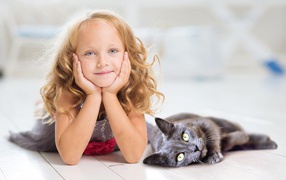 Маленькая милая голубоглазая девочка лежит на полу с котом
