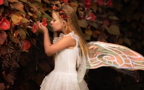 Маленькая девочка в костюме феи стоит у цветов