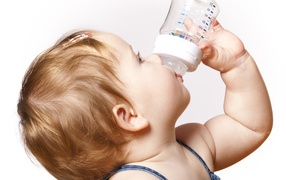 Little girl drinks milk from a bottle on a white background