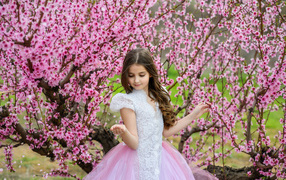 Маленькая девочка в красивом платье у дерева с розовыми цветами