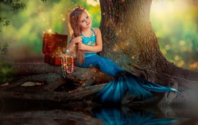 Маленькая девочка в костюме русалочки сидит у воды 