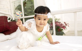 Маленькая девочка в белом платье с леденцом в руке