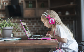 Little girl in headphones sits at a laptop