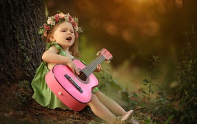 Little girl with a guitar under a tree