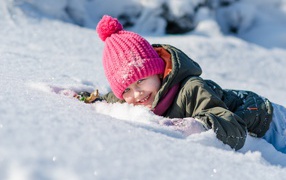 Маленькая улыбающаяся девочка лежит на снегу