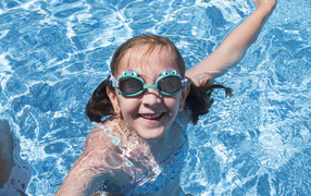 Маленькая улыбающаяся девочка в очках в бассейне 