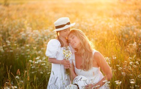 Мать с дочерью на поле с белыми ромашками в лучах солнца 
