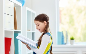 Умная девочка школьница с книгой в библиотеке 