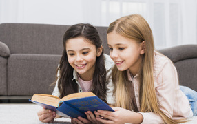 Две маленькие девочки читают книгу на полу