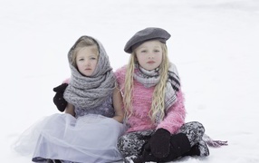 Two little sisters sit in the snow