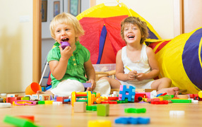 Два улыбающихся ребенка играют с конструктором 
