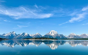View of snow-capped mountains under blue skies by the lake, Grand Teton National Park, Wyoming. USA