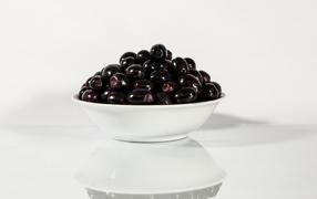 Black olives in a white plate are reflected in the surface