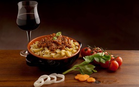 Pasta with minced meat on a table with a glass of wine and tomatoes