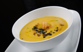 Желтый суп пюре в белой тарелке на черном фоне