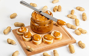Nut butter on the table with loaf and peanuts