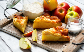 Куски пирога на столе с яблоками и мукой