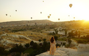 A girl stands on the edge of a cliff against the background of the sky with balloons