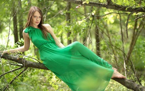Молодая девушка в зеленом платье лежит на ветке дерева