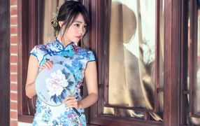 Девушка азиатка в красивом платье стоит у окна 