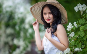 Asian girl in a big hat by a green bush