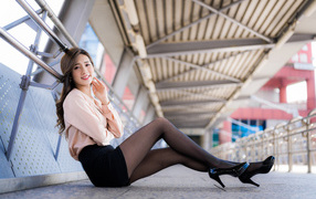 Девушка азиатка в черной юбке сидит в переходе 