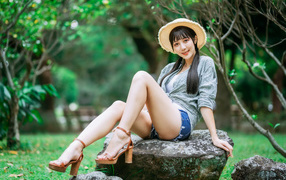Девушка азиатка в шляпе сидит на камне