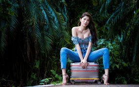 Asian girl in jeans sits on a suitcase