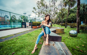 Девушка азиатка в джинсах сидит в парке 