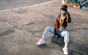 Asian girl sitting on a skateboard on the pavement