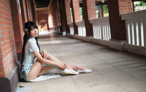 Девушка азиатка сидит на холодном полу у стены