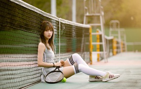 Девушка азиатка с тенистой ракеткой сидит у сетки