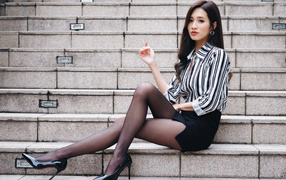 Красивая девушка азиатка в юбке сидит на ступеньках