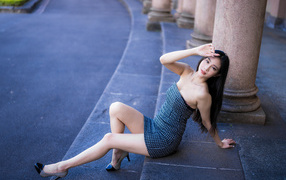 Красивая девушка азиатка в сером платье сидит на ступеньках