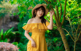 Красивая девушка азиатка в желтом платье   шляпе у дерева