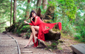 Красивая азиатка в красном платье сидит на дереве 