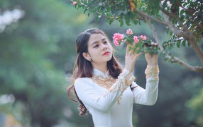 Красивая азиатка в белом платье у ветки с розовыми цветами
