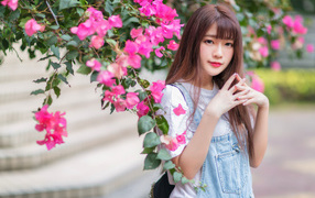 Красивая милая азиатка стоит у куста с розовыми цветами