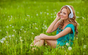 Красивая девушка с наушниками на голове  сидит на траве
