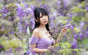 Brown-eyed Asian woman by a bush with wisteria flowers