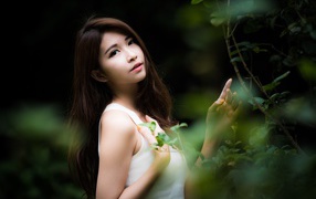 Cute asian woman in white stands by green leaves