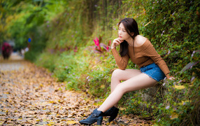 Задумчивая азиатка сидит в парке осенью 